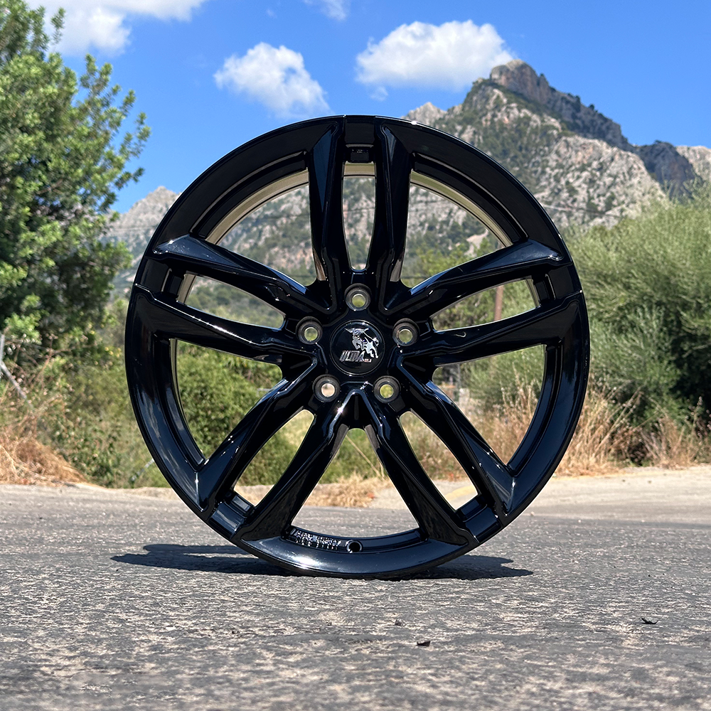 A sleek black alloy wheel set against a scenic backdrop of mountains and blue sky.