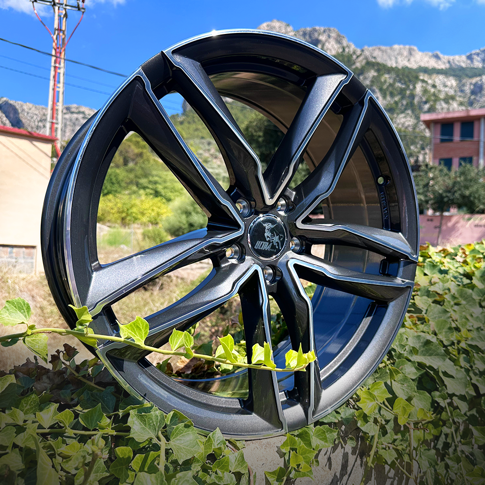 A close-up of a sleek car wheel displayed against a backdrop of greenery and buildings.