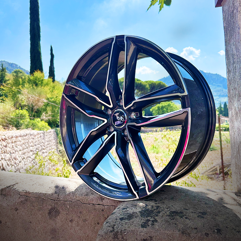A close-up of a sleek black alloy wheel resting on a stone surface with a scenic background.